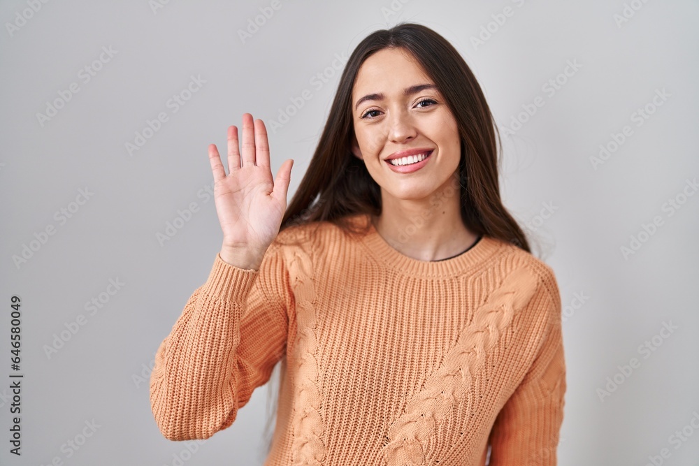 Young brunette woman standing over white background waiving saying hello happy and smiling, friendly welcome gesture Young brunette woman standing over white background waiving saying hello happy and smiling, friendly welcome gesture