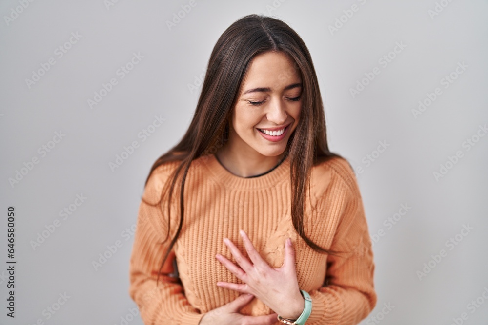 Obraz premium Young brunette woman standing over white background smiling and laughing hard out loud because funny crazy joke with hands on body.