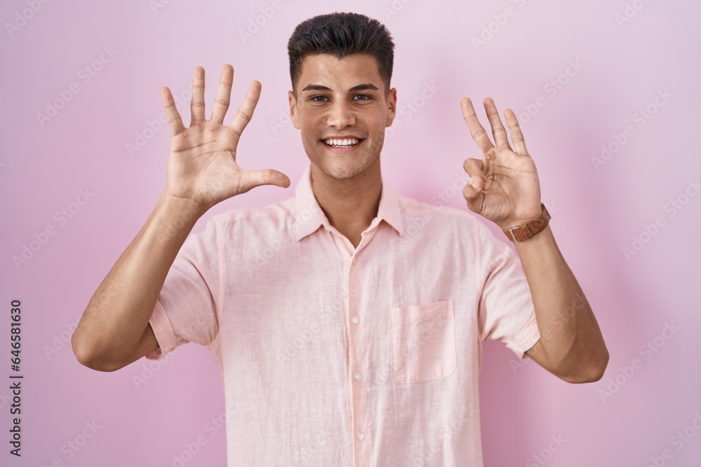 Young hispanic man standing over pink background showing and pointing up with fingers number eight while smiling confident and happy. Young hispanic man standing over pink background showing and pointing up with fingers number eight while smiling confident and happy.
