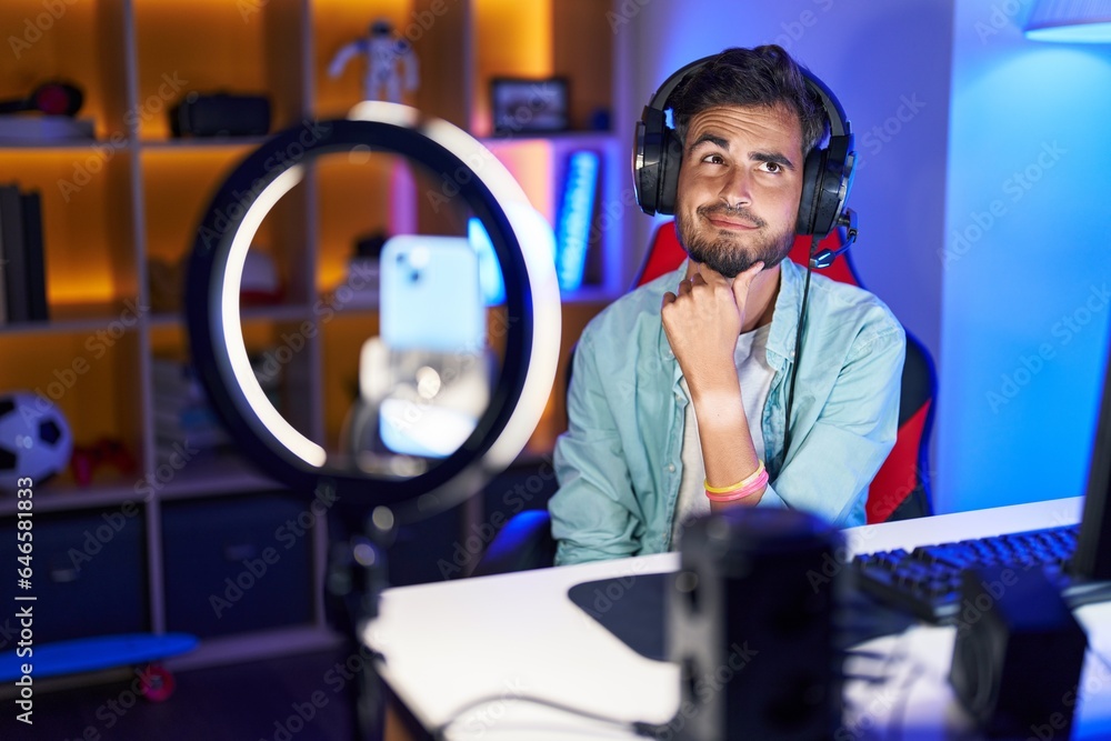 Young hispanic man with tattoos recording tutorial with smartphone smiling looking confident at the camera with crossed arms and hand on chin. thinking positive.