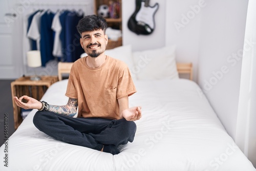 Young hispanic man doing yoga exercise sitting on bed at bedroom