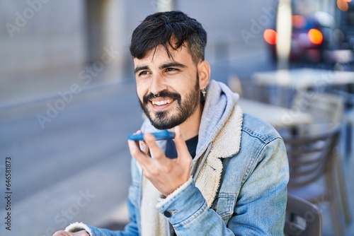 Young hispanic man talking on smartphone sitting on table at coffee shop terrace