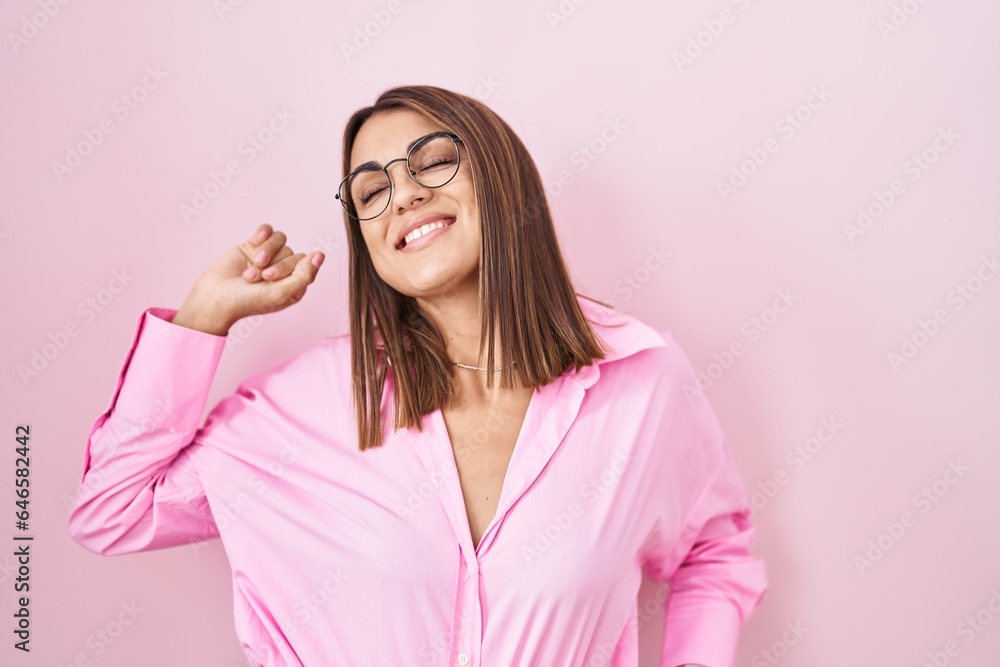 Young hispanic woman wearing glasses standing over pink background stretching back, tired and relaxed, sleepy and yawning for early morning Young hispanic woman wearing glasses standing over pink background stretching back, tired and relaxed, sleepy and yawning for early morning