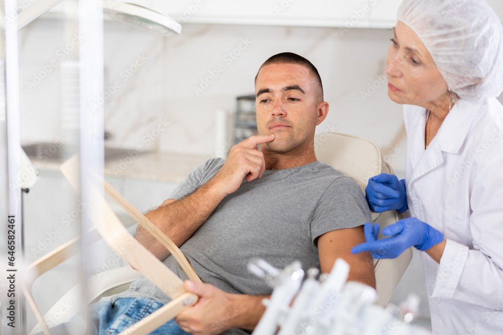 Obraz premium Man looks in the mirror and consults a professional female plastic surgeon