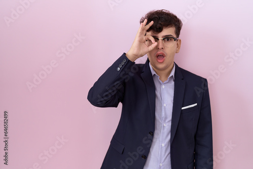 Young non binary man with beard wearing suit and tie doing ok gesture shocked with surprised face, eye looking through fingers. unbelieving expression. © Krakenimages.com