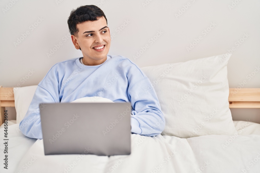 Young non binary man using laptop sitting on bed Young non binary man using laptop sitting on bed