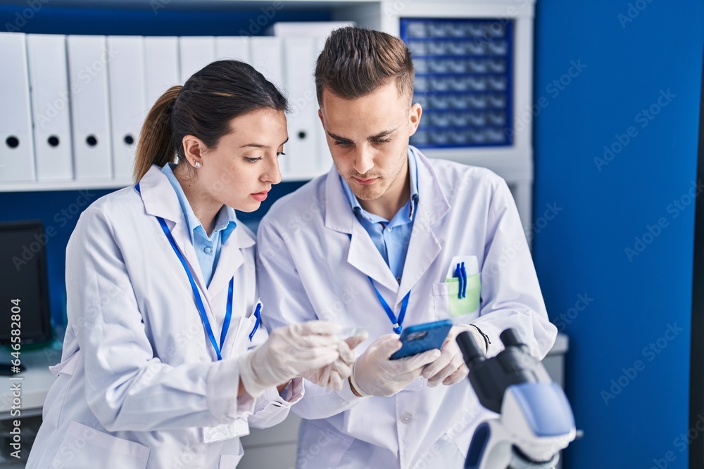 Man and woman scientists using smartphone looking sample at laboratory Man and woman scientists using smartphone looking sample at laboratory
