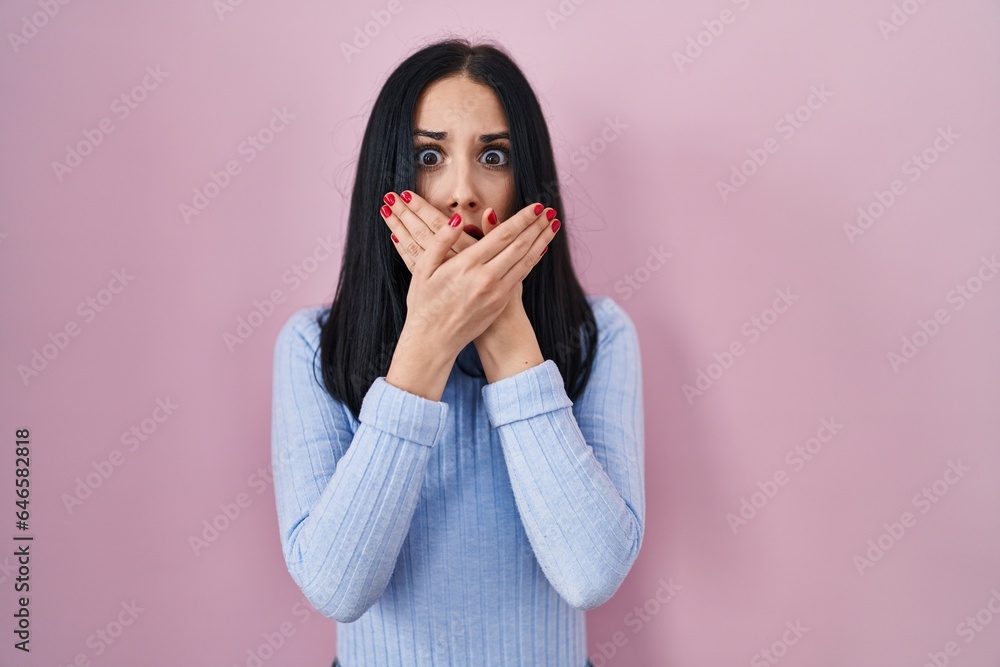 Hispanic woman standing over pink background shocked covering mouth with hands for mistake. secret concept. Hispanic woman standing over pink background shocked covering mouth with hands for mistake. secret concept.
