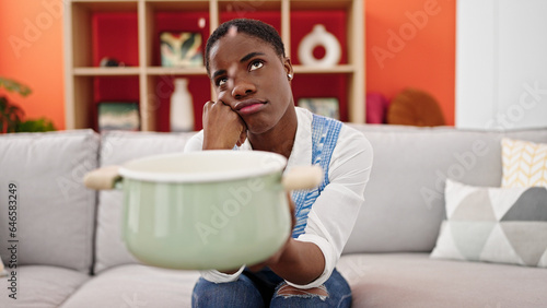 African american woman holding cooking pot for water leak at home