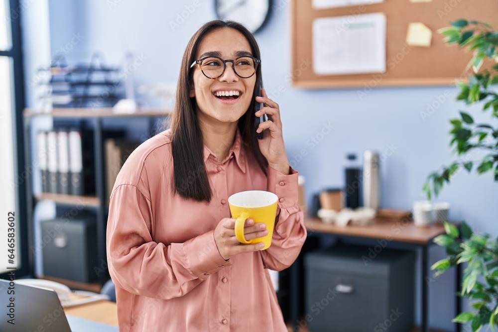 Young hispanic woman business worker talking on smartphone drinking coffee at office Young hispanic woman business worker talking on smartphone drinking coffee at office