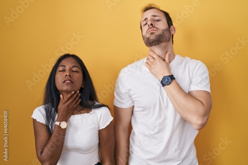 Interracial couple standing over yellow background touching painful neck, sore throat for flu, clod and infection