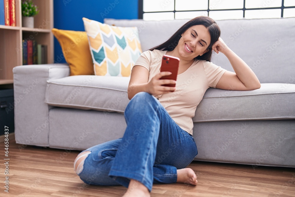 Young beautiful hispanic woman using smartphone sitting on floor at home Young beautiful hispanic woman using smartphone sitting on floor at home