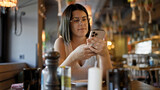 Young beautiful hispanic woman using smartphone sitting on the table at the restaurant