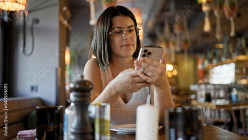 Young beautiful hispanic woman using smartphone sitting on the table at the restaurant