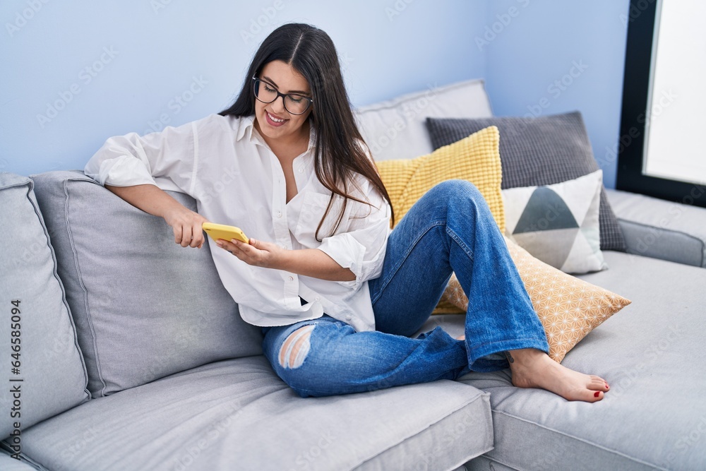 Young hispanic woman using smartphone sitting on sofa at home Young hispanic woman using smartphone sitting on sofa at home