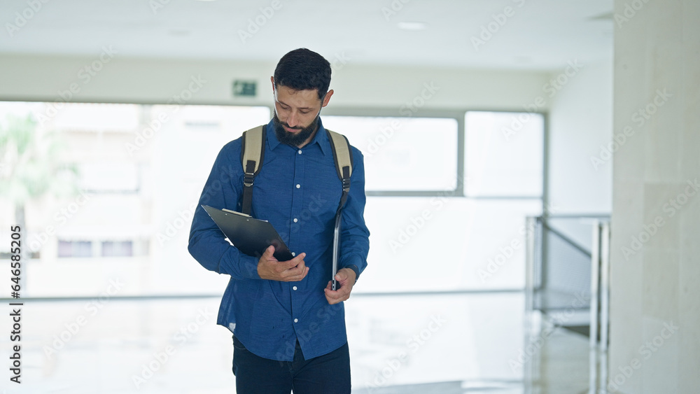 Young hispanic man business worker holding clipboard and laptop walking at the office Young hispanic man business worker holding clipboard and laptop walking at the office
