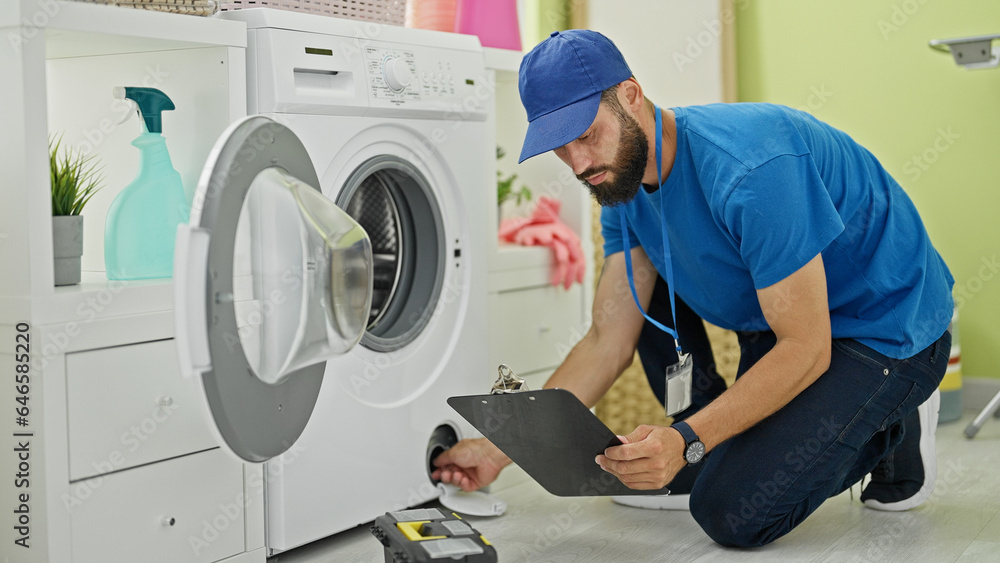 Young hispanic man technician repairing washing machine reading instructions at laundry room Young hispanic man technician repairing washing machine reading instructions at laundry room