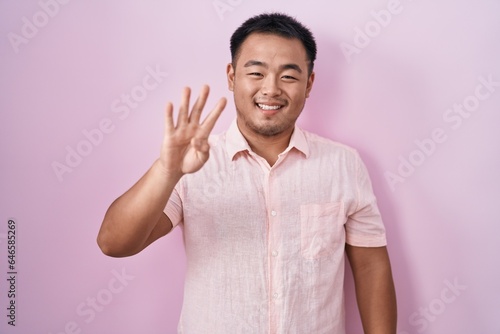 Chinese young man standing over pink background showing and pointing up with fingers number four while smiling confident and happy.