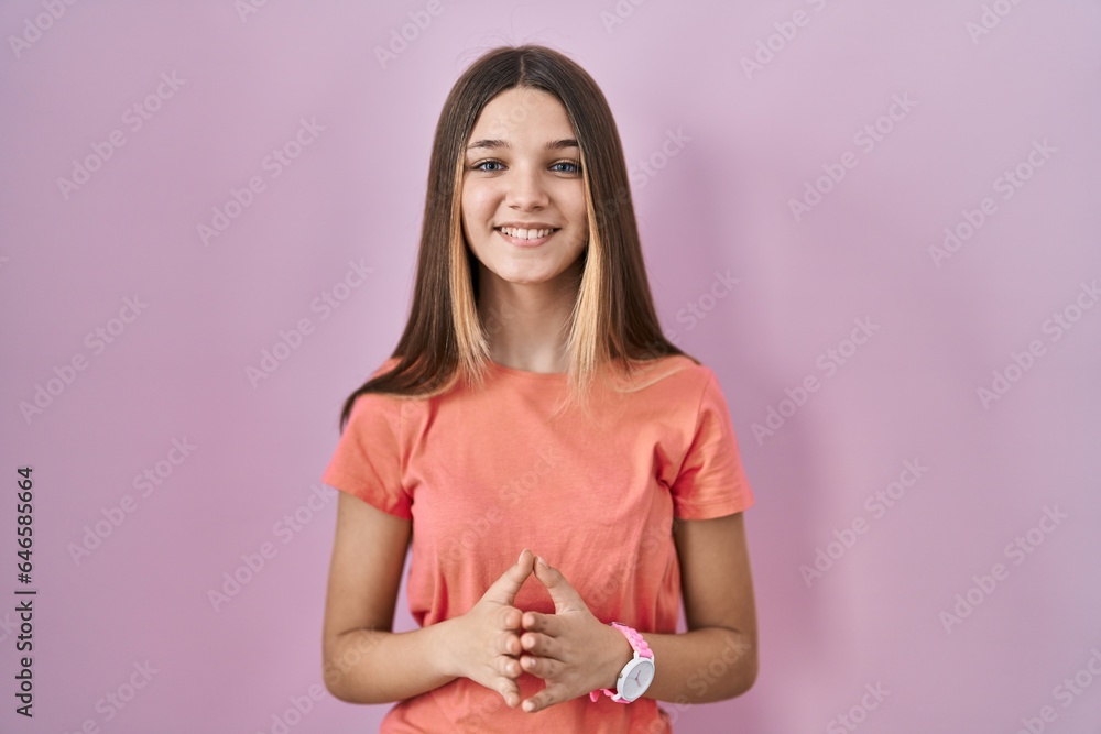 Teenager girl standing over pink background hands together and fingers crossed smiling relaxed and cheerful. success and optimistic Teenager girl standing over pink background hands together and fingers crossed smiling relaxed and cheerful. success and optimistic