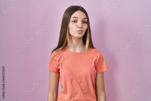 Teenager girl standing over pink background looking at the camera blowing a kiss on air being lovely and sexy. love expression.