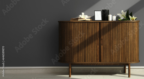 Mortuary urn with blank photo frame, glowing candles and lily flowers on commode in room. Banner for design © Pixel-Shot