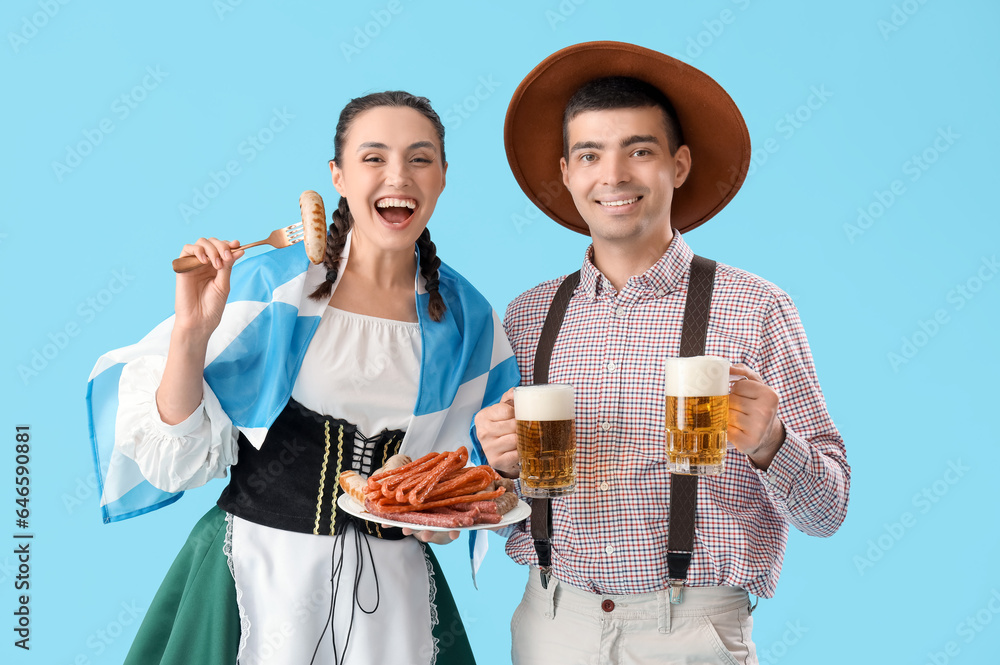 Young couple in traditional German clothes with beer and snacks on blue background Young couple in traditional German clothes with beer and snacks on blue background