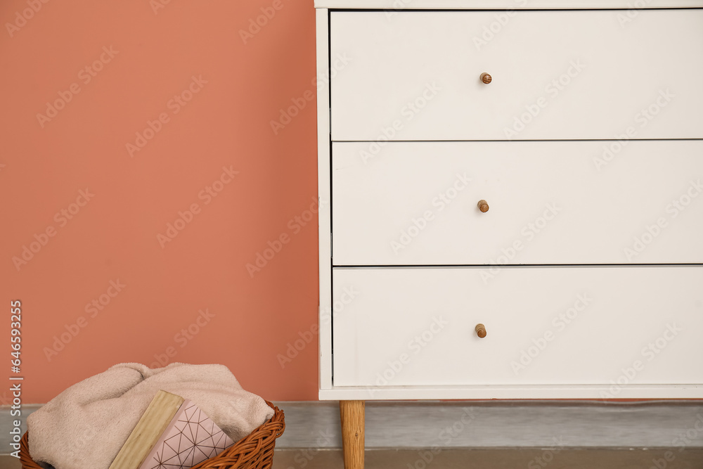 Fototapeta premium Stylish chest of drawers and basket with plaid near color wall, closeup