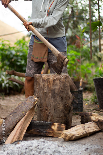 Persona partiendo leña con un hacha sobre un tronco en un patio de México. photo