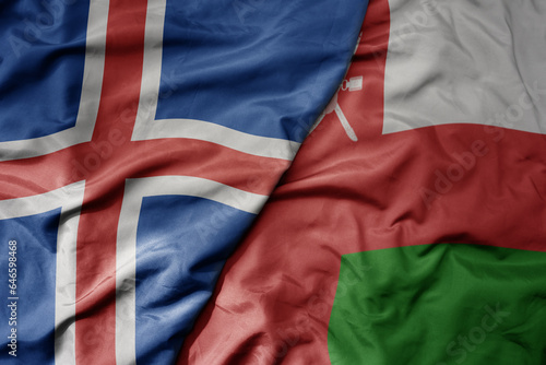 big waving national colorful flag of icelandic and national flag of oman .