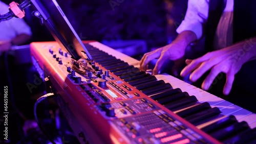 Closeup of piano player's hands slow motion playing keyboard. Red and purple lighting, live music performance