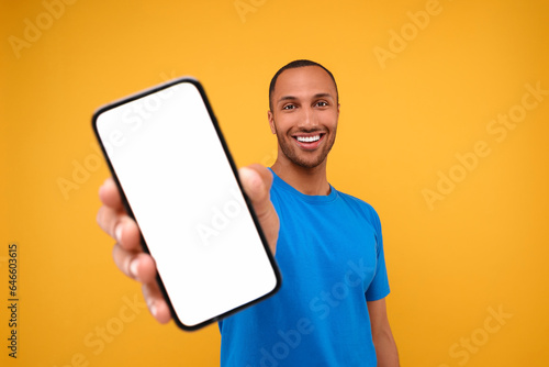 Young man showing smartphone in hand on yellow background