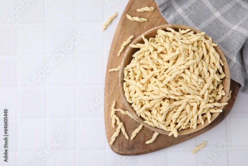 Bowl with uncooked Italian trofie pasta on white tiled table, flat lay. Space for text photo