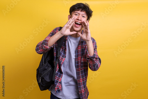Excited Asian male students carrying backpak shout out front to camera, showing announcing gesture photo