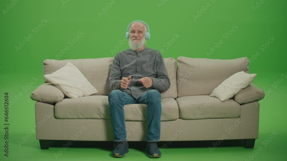 Green Screen. A Happy Old Man with a Gray Beard Listens to Music on Headphones. An Elderly Man Sitting on a Sofa Dances to Music in Headphones. Emerging Technologies for Seniors. Green Screen. A Happy Old Man with a Gray Beard Listens to Music on Headphones. An Elderly Man Sitting on a Sofa Dances to Music in Headphones. Emerging Technologies for Seniors.