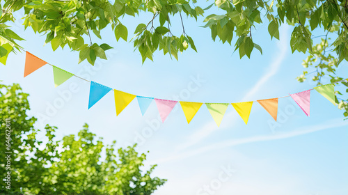 colorful pennant string decoration in green tree foliage on blue sky, summer party background template banner with copy space