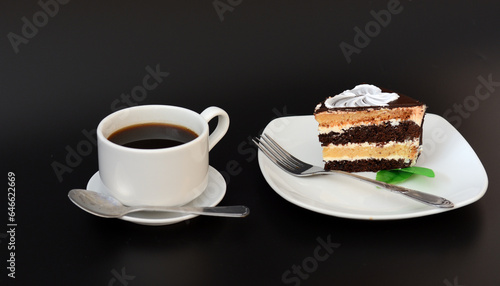 A piece of biscuit chocolate cake on a plate and a cup of hot black background.