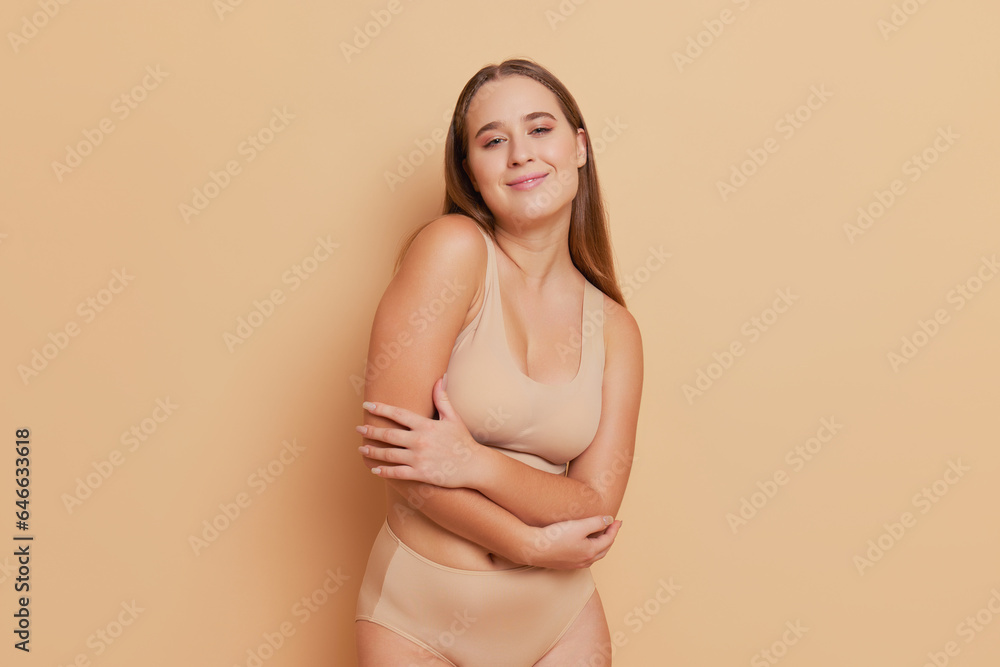 Pretty female model girl in flesh-colored negligee hugging herself with sweet smile over background, best underwear concept, copy space Pretty female model girl in flesh-colored negligee hugging herself with sweet smile over background, best underwear concept, copy space