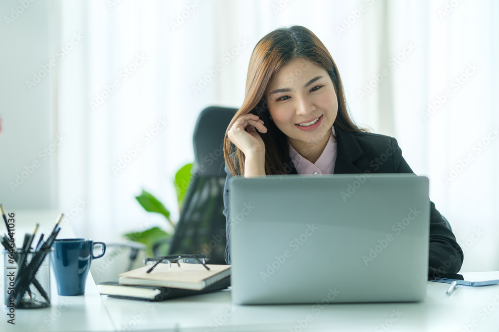 Attractive asian businesswoman in black suit sitting at office desk and using laptop computer. Attractive asian businesswoman in black suit sitting at office desk and using laptop computer.
