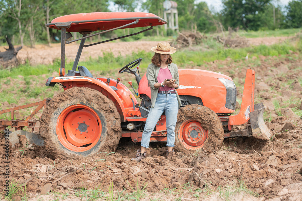 Attractive farmer, Young woman with tablet standing on field in sunset while tractor baling in background, High technology innovations for increasing productivity in agriculture. Attractive farmer, Young woman with tablet standing on field in sunset while tractor baling in background, High technology innovations for increasing productivity in agriculture.