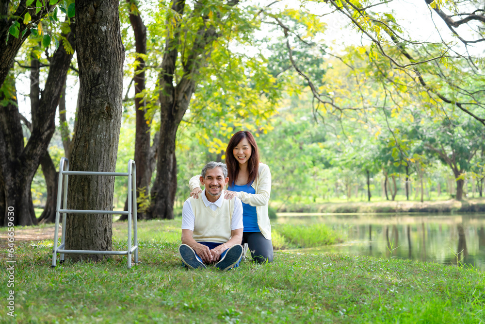 happy family,senior disability father sitting on grasses with a walker beside,young adult daughter sitting behind him doing massage on shoulder,both of them smiling happily on holiday in springtime happy family,senior disability father sitting on grasses with a walker beside,young adult daughter sitting behind him doing massage on shoulder,both of them smiling happily on holiday in springtime
