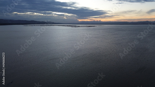 Aerial view over the water of the lake with sunset views and sun reflections. Aerial view of lake. Flying over water. Flight over calm lake surface