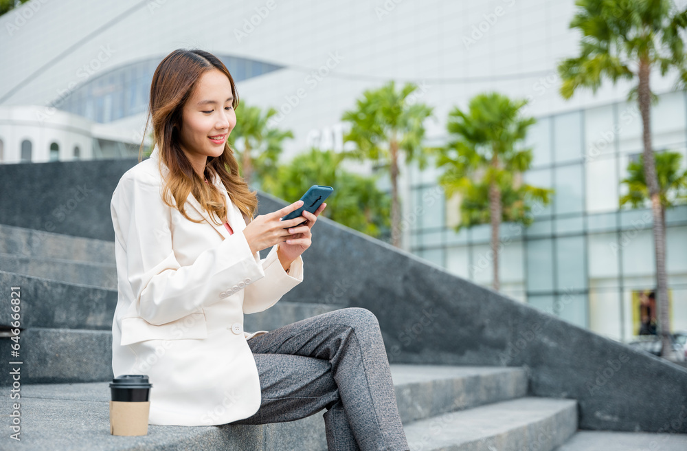 Lifestyle woman business people using mobile smart phones in the city outdoors office building. Young Asian female wearing blue shirt while use cellphone with holding coffee cup sitting on staircase Lifestyle woman business people using mobile smart phones in the city outdoors office building. Young Asian female wearing blue shirt while use cellphone with holding coffee cup sitting on staircase