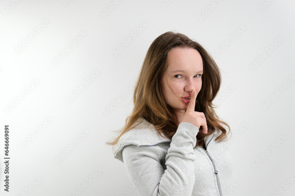 a young teenage girl puts her finger to her lips secrecy don't tell anyone sharply turn around look into the frame wave a finger negatively. on a white background stern look a young teenage girl puts her finger to her lips secrecy don't tell anyone sharply turn around look into the frame wave a finger negatively. on a white background stern look