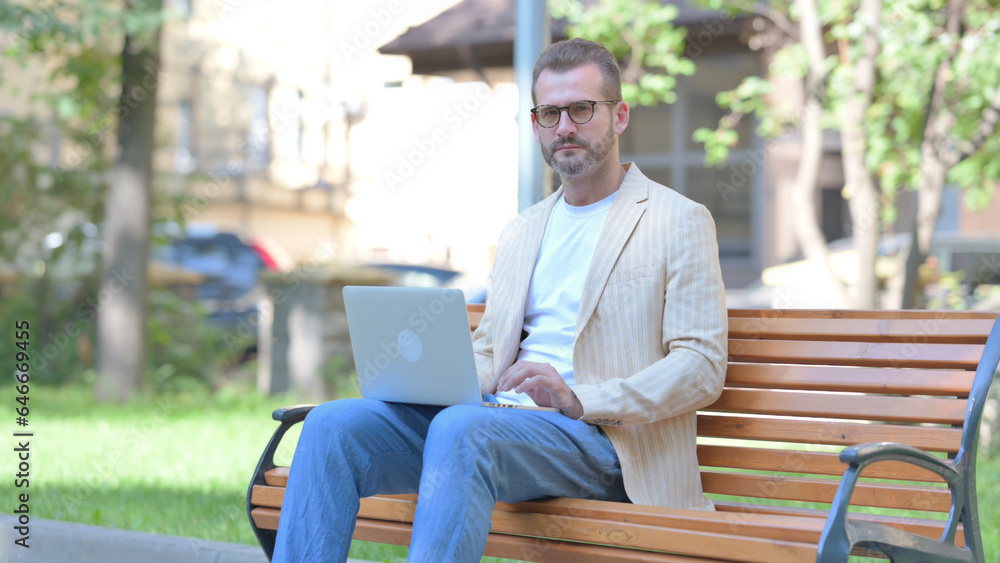 Fototapeta premium Middle Aged Man Looking at Camera while Working on Laptop Outdoor
