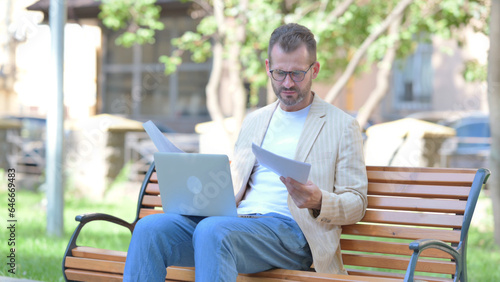 Middle Aged Man Feeling Upset while Reading Contract and Using Laptop Outdoor