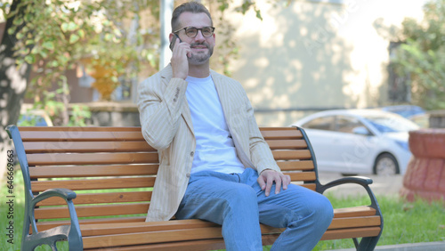 Modern Casual Man Talking on phone while Sitting Outdoor on a Bench