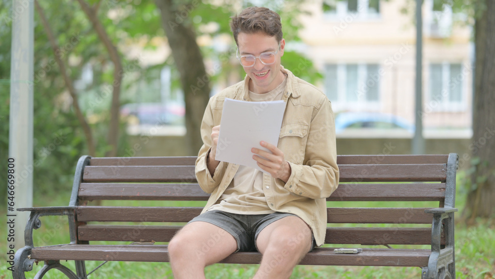 Casual Young Man Celebrating while Reading Documents while Sitting Outdoor Casual Young Man Celebrating while Reading Documents while Sitting Outdoor