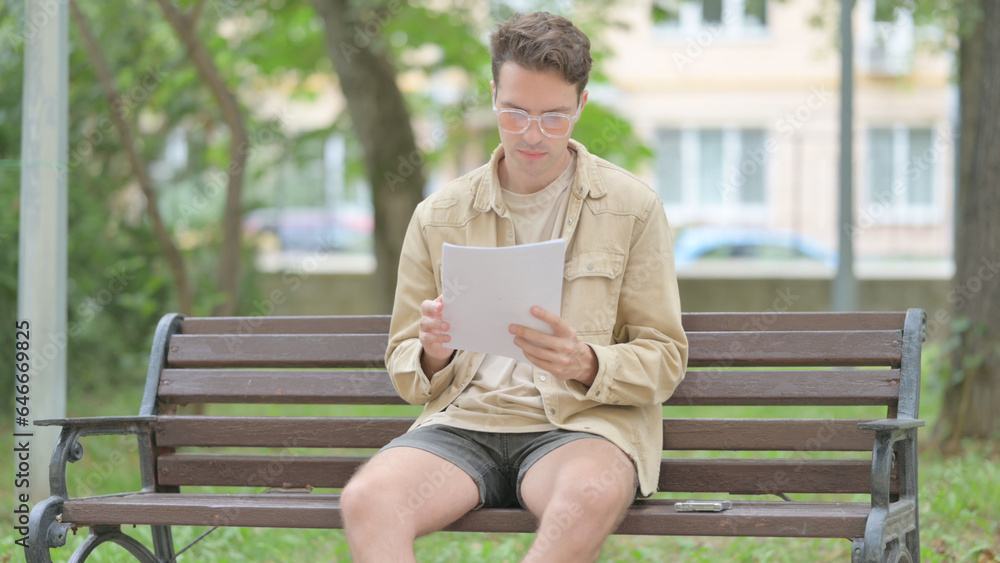 Obraz premium Casual Young Man Reading Documents while Sitting Outdoor