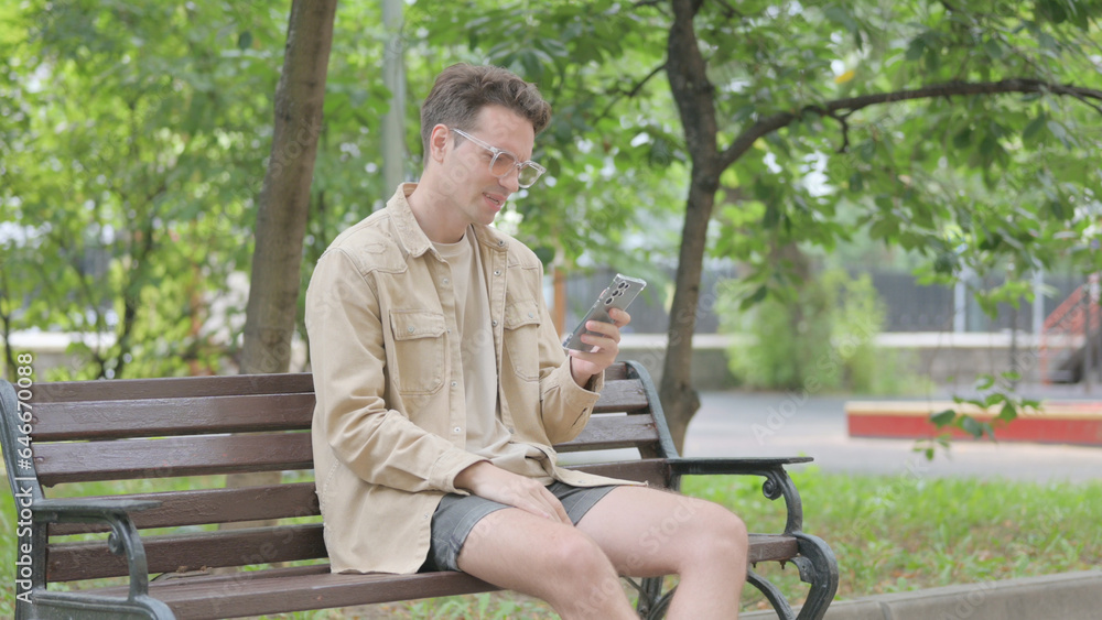 Fototapeta premium Modern Young Man Facing Loss on Smartphone while Sitting on Bench