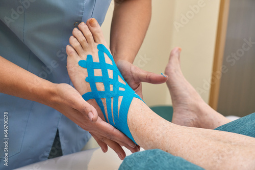 Female doctor applying blue kinesio tape on woman s foot